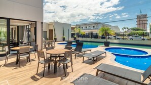 A rooftop pool area with lounge chairs and tables, a clear view of the sky, and a building in the background. - Condominium w/ Pool, 450 m fr/ the sea and 650 m fr/ Beto Carrero World - Lavs (Penha)