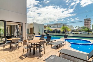 A rooftop pool area with lounge chairs and tables, a clear view of the sky, and a building in the background. - Condominium w/ Pool, 450 m fr/ the sea and 650 m fr/ Beto Carrero World - Lavs (Penha)