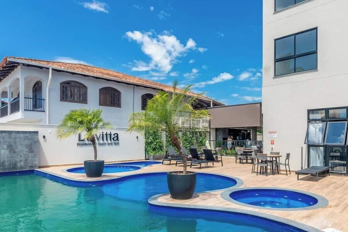 Zona de piscina amb gandules, una palmera i un edifici amb un rètol que diu 'Lavitta Residencia Beach and Park'.