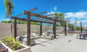 Una terraza en la azotea con una pérgola de madera, un sofá modular, una silla colgante y un comedor.