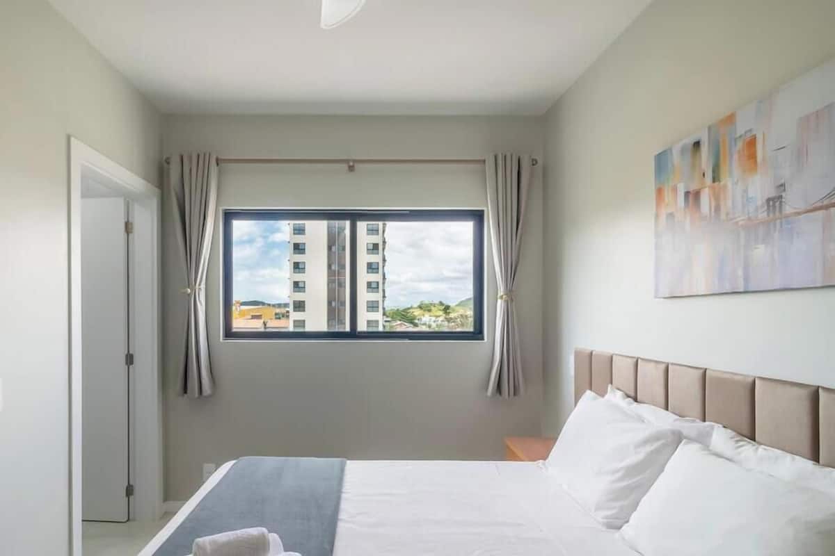 Habitació d'hotel amb llit, finestra amb cortines, quadre a la paret i porta.