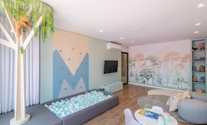 Una sala de estar moderna con un área de juegos, un televisor montado y una pared decorada con un mural de temática natural.