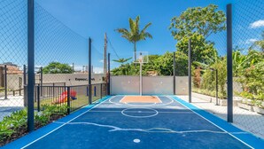 An outdoor basketball court with a chain-link fence, basketball hoop, and surrounding greenery. - Condominium w/ Pool, 450 m fr/ the sea and 650 m fr/ Beto Carrero World - Lavs (Penha)