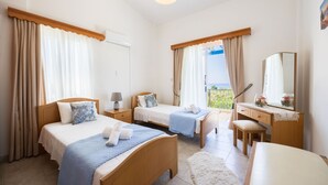 A hotel room with two beds, a desk, a chair, and a view of the sea. - Lemon Grove Villa Ena (Argaka)