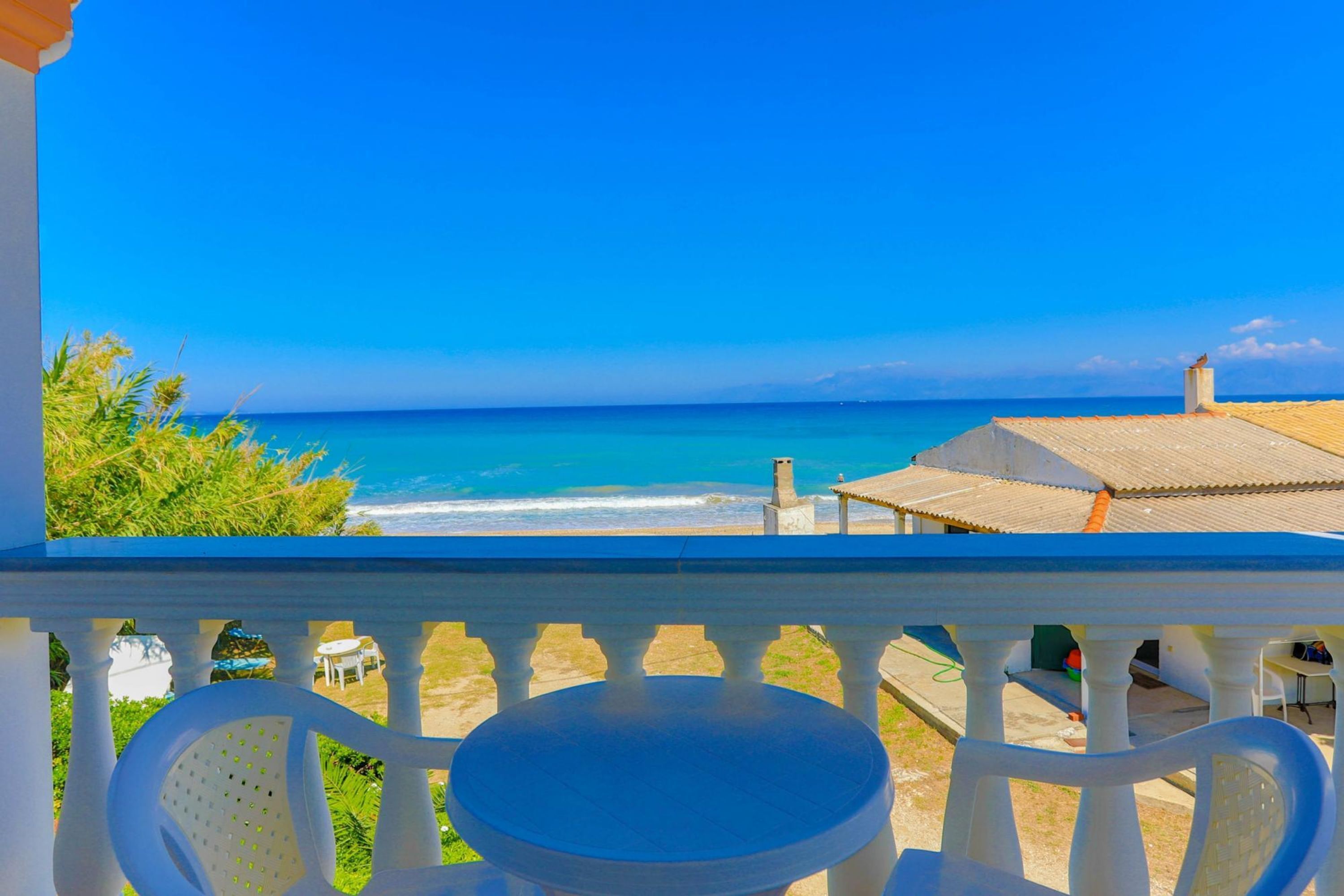 A balcony with a view of the ocean, a table, and chairs.