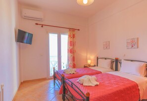 A hotel room with two beds, a TV, a window with curtains, and a balcony. - Beach Villa Vasso Dio (Acharavi)