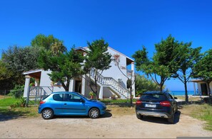 A two-story building with a white facade and a balcony. There are two cars parked in front. - Beach Villa Vasso Dio (Acharavi)