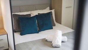 A neatly made bed with a patterned bedspread, a folded white towel, and two teal pillows. - Modern 3 Bed Home with Garden, Free Parking, Wi-Fi (Lazenby)