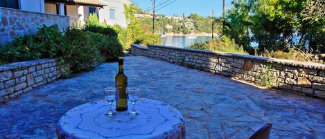 A stone patio with a table set for two, overlooking a body of water and a hillside.