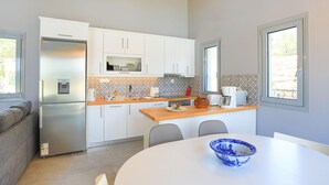 A modern kitchen with white cabinets, a stainless steel refrigerator, a wooden countertop, and a dining table with a blue bowl. - Villa Christina in Poulades (Poulades)