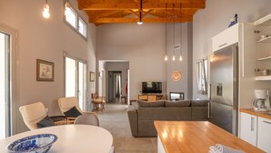 A spacious living area with a wooden ceiling, a kitchen with a refrigerator, a dining table, and a TV. - Villa Christina in Poulades (Poulades)