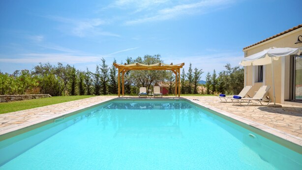 A swimming pool with a pergola, lounge chairs, and a building with a tiled roof. - Villa Christina in Poulades (Poulades)