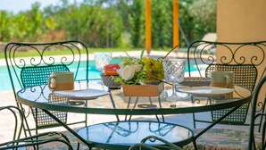 A round glass table with metal chairs, a bowl of fruit, and a vase of flowers. - Villa Christina in Poulades (Poulades)