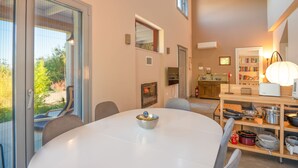 A modern kitchen with a built-in oven, a dining area with a round table, and a bookshelf filled with books. - Villa Aphrodite in Poulades (Poulades)