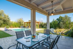 Une terrasse extérieure avec une table en verre, des chaises et une piscine en arrière-plan.