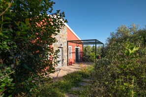 Un bâtiment rustique à la façade en pierre et au toit rouge, entouré d’une végétation luxuriante.