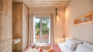 A bedroom with a large bed, a wooden wardrobe, a sliding glass door to a balcony, and a small bedside table with a lamp. - Villa Aphrodite in Poulades (Poulades)