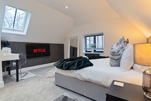 A modern bedroom with a bed, a TV mounted on the wall, a desk, and a window. - High Trees Lodge – Luxury Retreat • 2 King Suites (Whitstable)