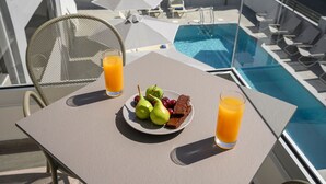 Ett bord med en tallrik full av frukt och choklad, två glas apelsinjuice och en plats vid poolen med parasoller och solstolar.