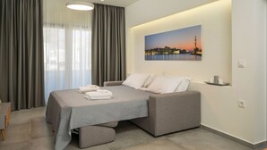 Ett modernt hotellrum med en säng, grå gardiner, en målning som föreställer en stadsbild och en liten hylla med ljus.