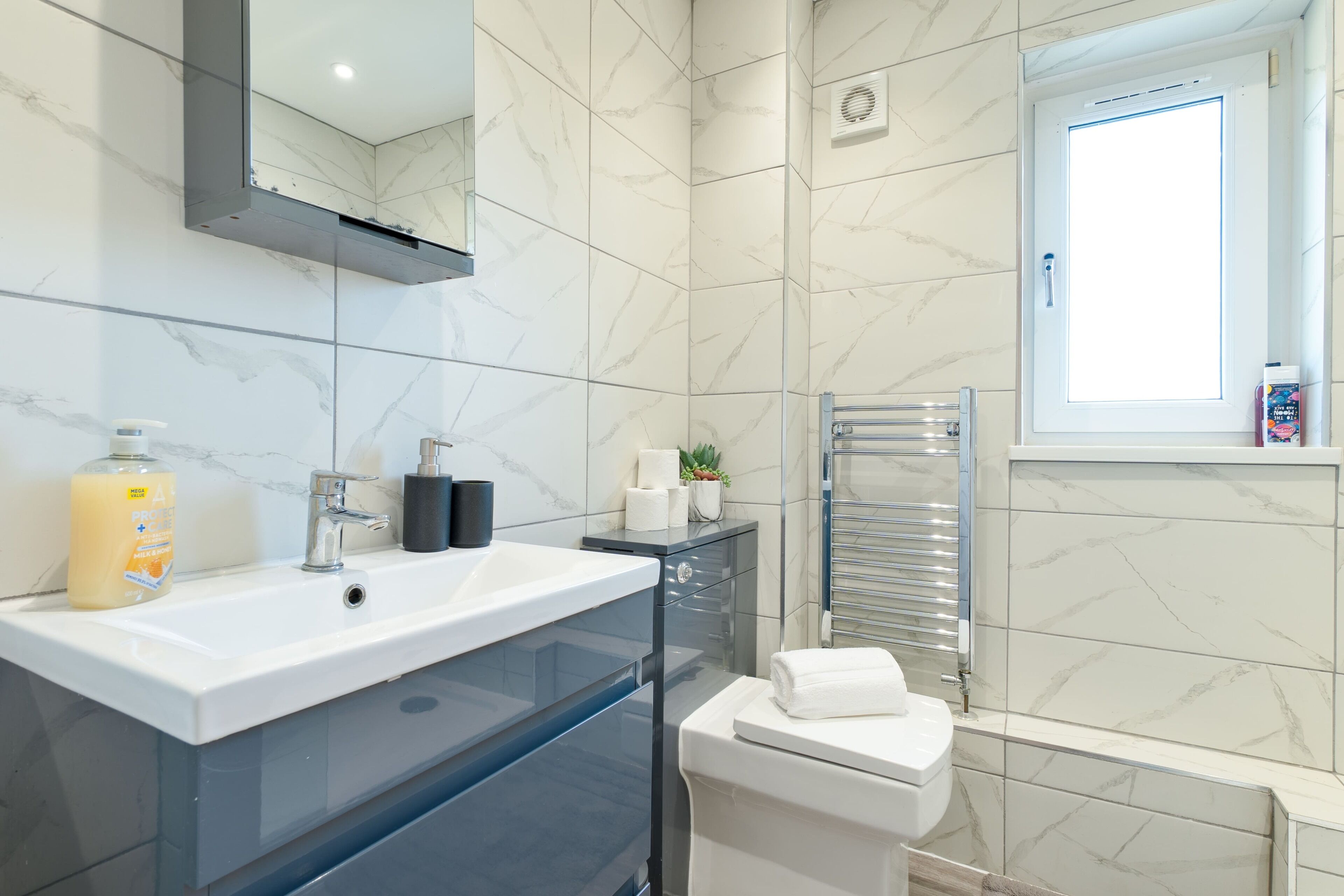 A modern bathroom with a white sink, a glass cabinet, a towel rack, and a window.