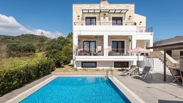 A modern two-story house with a swimming pool, outdoor seating, and a scenic hillside view.