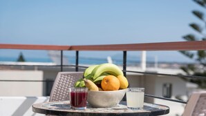 A table with a bowl of fruit and two glasses on a balcony overlooking a cityscape.