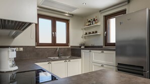 A modern kitchen with white cabinets, a stainless steel refrigerator, a coffee maker, and a built-in oven.