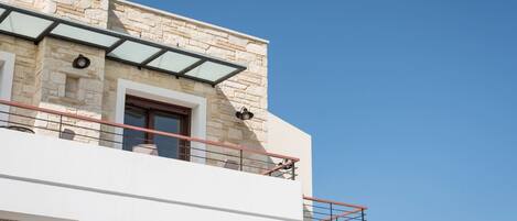 A modern building with stone facade, a glass balcony, and a clear blue sky.