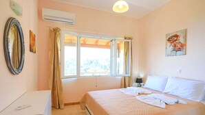 Une chambre à coucher comprenant un lit, une table de chevet, un appareil de climatisation, une fenêtre avec des rideaux et un tableau accroché au mur.