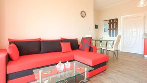 Un salon moderne avec un canapé rouge, une table basse en verre et un coin repas comprenant une table et des chaises blanches.