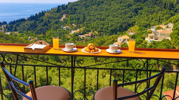 Un balcon avec une table dressée pour le petit-déjeuner, offrant une vue sur une colline verdoyante et la mer.