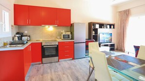 Une cuisine compacte avec des meubles rouges, des appareils en acier inoxydable et une table à manger en verre.