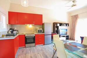 A compact kitchen with red cabinets, stainless steel appliances, and a glass dining table. - Eros Sea View in Kentroma (Rachi)