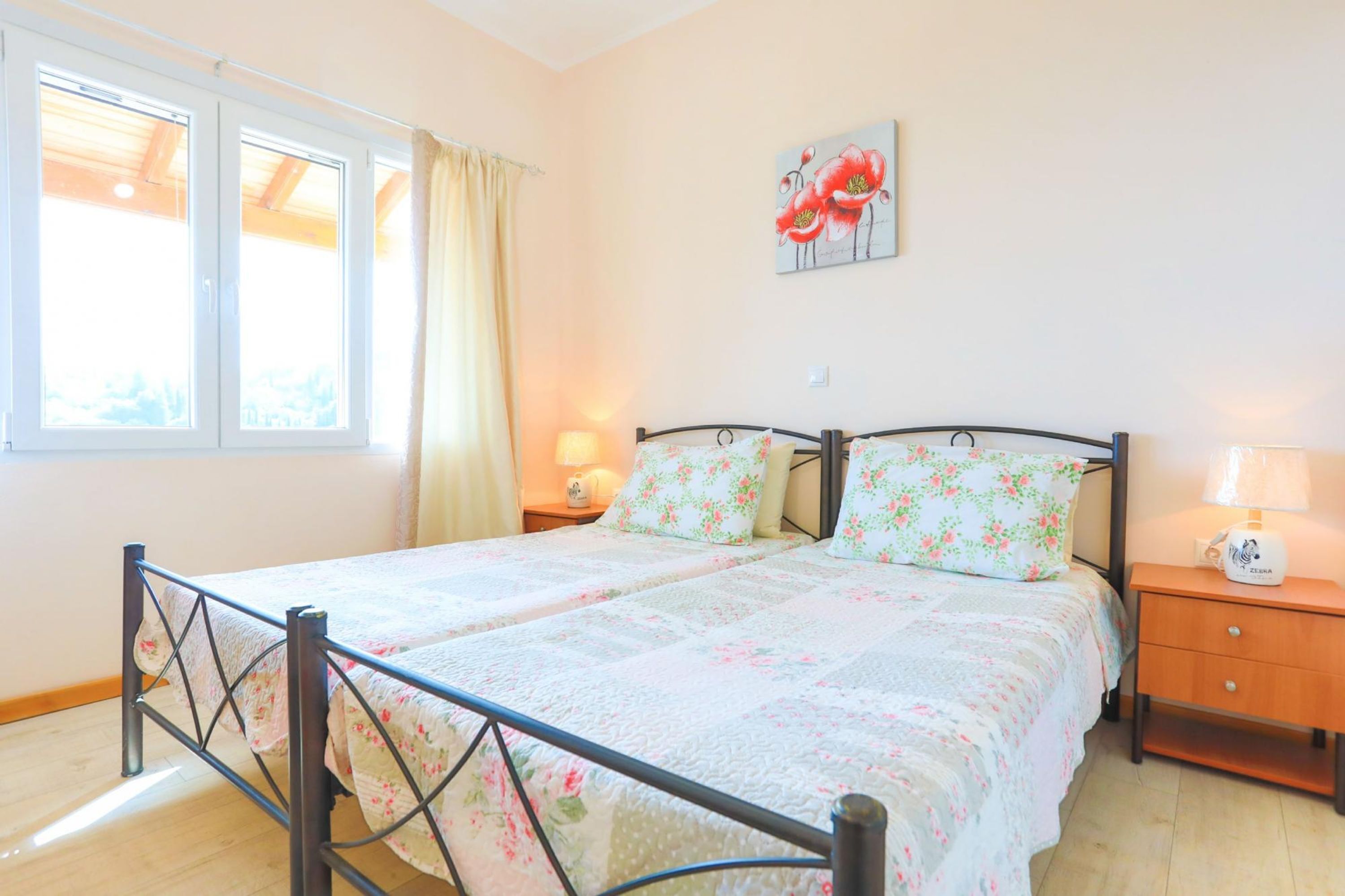 Una cama doble con ropa de cama floral, una mesita de noche con una lámpara y una ventana con cortinas.