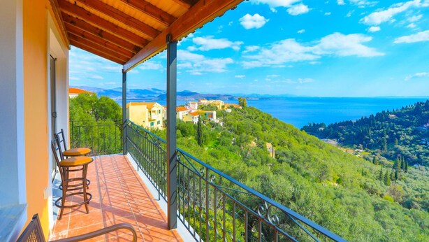 Un balcon agrémenté d’une pergola en bois, de deux chaises et offrant une vue sur un paysage côtier avec des bâtiments et de la végétation.