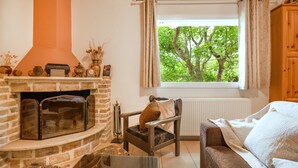 Een gezellige woonkamer met een open haard, een raam met uitzicht op bomen, een houten stoel en een bank.