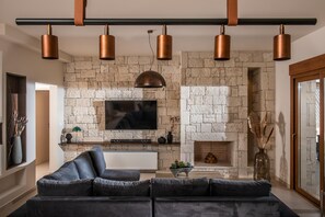 A living room with a stone fireplace, a flat-screen TV mounted above it, and a modern sofa. - Alpha House in Crete (Ligaria)