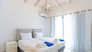 A double bed with white linens and blue towels, a white nightstand, and a ceiling fan. - Villa Loki in Kremithas (Kremithas)