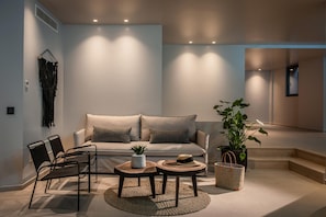 A modern living room with a sofa, two round tables, a chair, a plant, and a staircase. - Made By The Sea Villa 5 (Mades)
