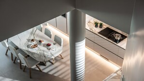 A modern dining area with a marble table and chairs, a kitchen with a built-in stove, and a large pillar. - Made By The Sea Villa 5 (Mades)