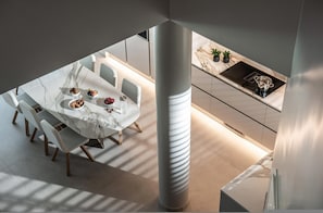 A modern dining area with a marble table and chairs, a kitchen with a built-in stove, and a large pillar. - Made By The Sea Villa 5 (Mades)