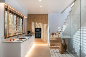 A modern kitchen with a built-in oven, a coffee maker, and a breakfast bar. There is a staircase leading to another level. - Made By The Sea Villa 4 (Mades)