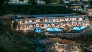 Ein modernes Hotel mit mehreren Schwimmbecken, einer Dachterrasse und einem angelegten Garten.