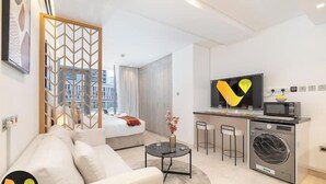 A modern hotel room with a bed, a sofa, a small round table, a TV, a microwave, and a washing machine. - Vogue | Sterling near Dubai Mall | Burj Khalifa (Dubai)