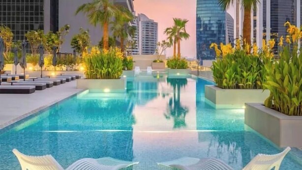 A pool area with lounge chairs and palm trees. - Vogue | Sterling near Dubai Mall | Burj Khalifa (Dubai)