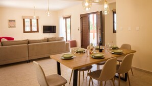 A dining area with a wooden table set for four, a sofa, and a TV mounted on the wall. - Villa Kerastis in Malatya (Malatya)