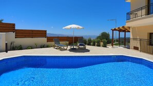 A swimming pool with lounge chairs and an umbrella, surrounded by a building with a balcony and a view of the mountains. - Villa Kerastis in Malatya (Malatya)