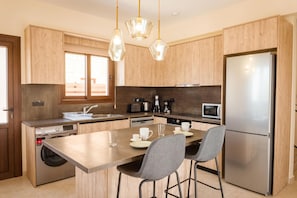 A modern kitchen with wooden cabinets, stainless steel appliances, a central island with chairs, and pendant lighting. - Villa Kerastis in Malatya (Malatya)