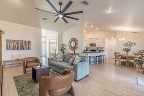 A spacious living area with a sofa, coffee table, and chairs, a kitchen in the background, and a ceiling fan. - Waterfront 4BR retreat w/ backyard (Cape Coral)